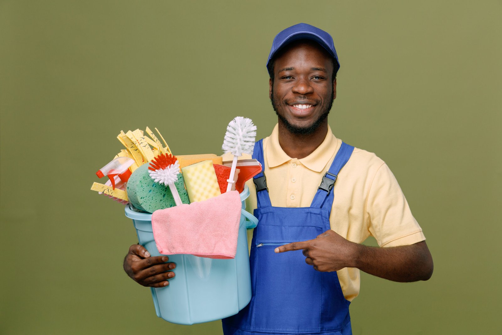 smiling holding and points at bucket of cleaning tools young africanamerican cleaner male in uniform with gloves isolated on green background